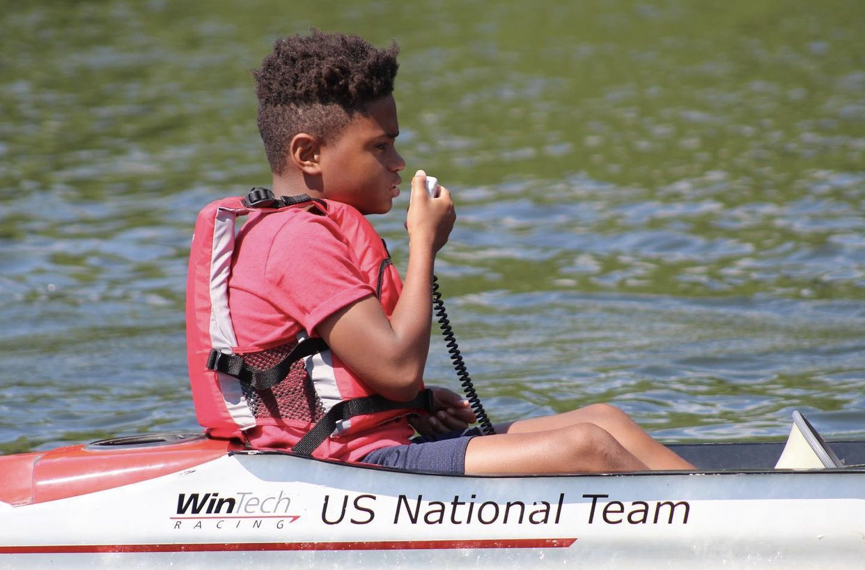 Young boy wearing life jacket holding a microphone to call commands to rowers